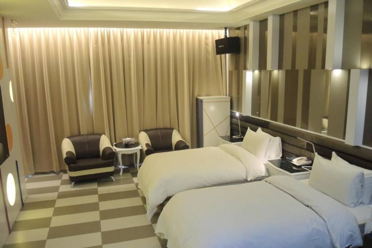 A hotel room with two beds, a sofa, a small table, and a TV.