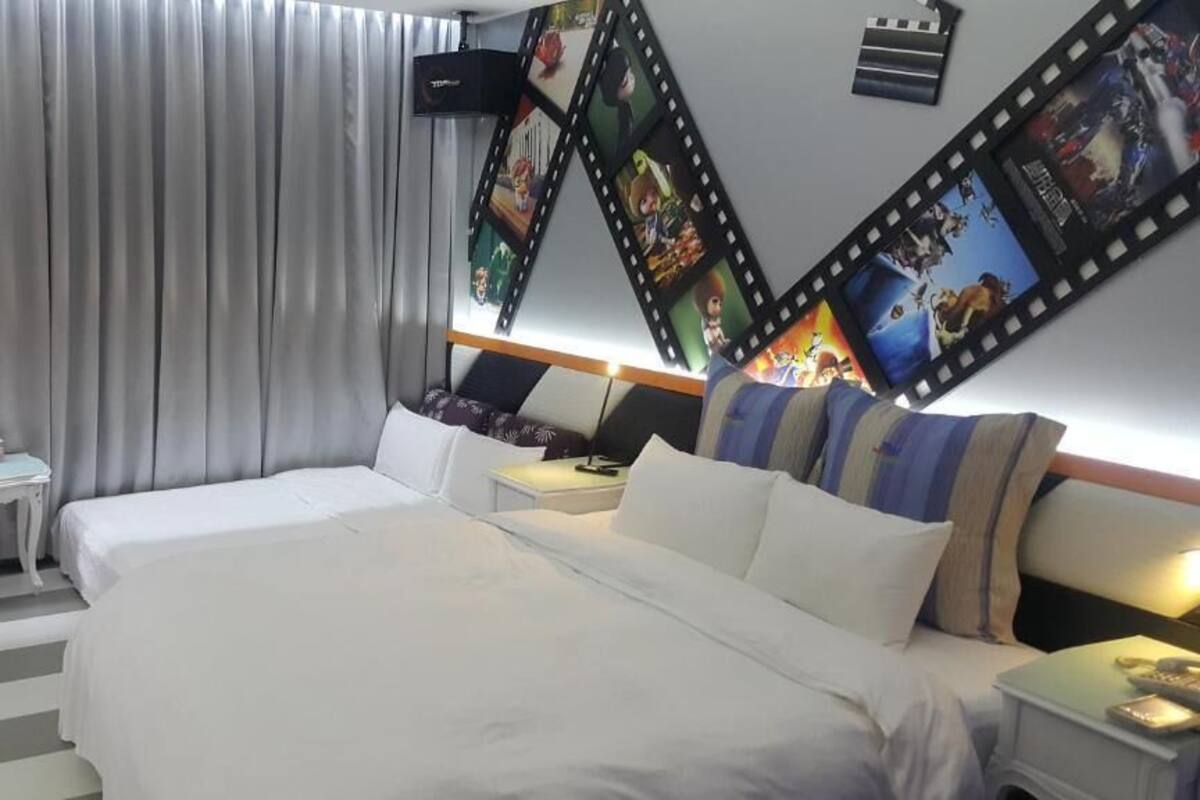 A hotel room with a large bed, a bedside table, a nightstand, and a wall decorated with film strips and movie posters.