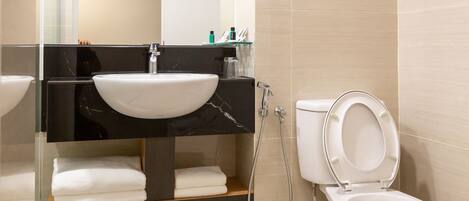 A modern bathroom with a glass-enclosed sink, a toilet with a raised seat, and a shower area.