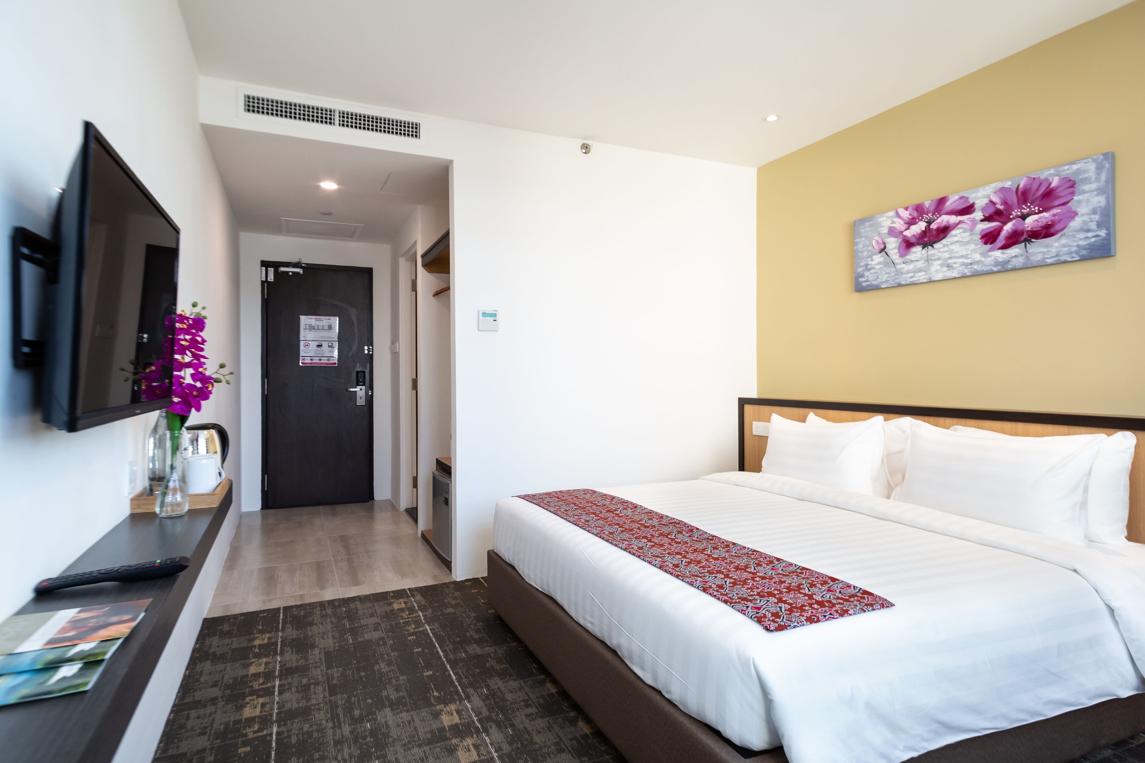 A hotel room with a bed, a TV, a desk, and a painting on the wall.