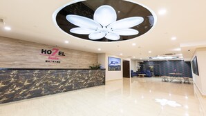 Een hotel receptie met een modern design, inclusief een grote plafondlamp in de vorm van een bloem, een receptiebalie en een zithoek met tafels en stoelen.