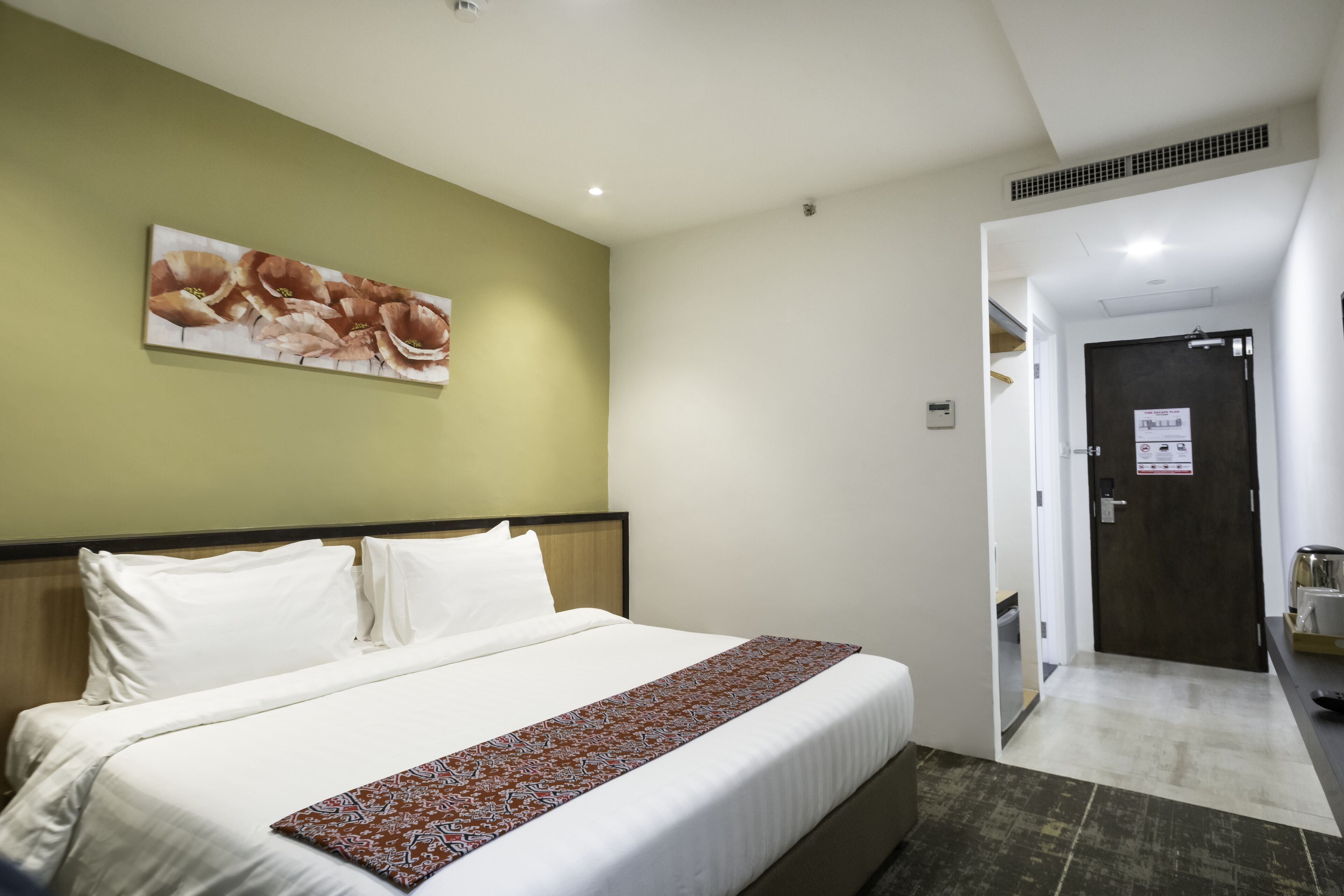 Une chambre d’hôtel avec un grand lit, un mur vert et une porte donnant sur le couloir.