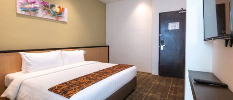 Una habitación de hotel con una cama grande, un cabecero de madera, un cuadro en la pared, una puerta y un televisor sobre un soporte.