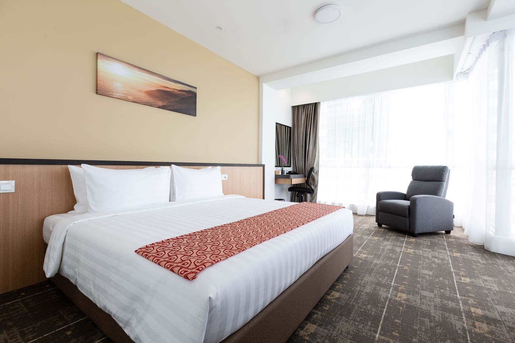A hotel room with a large bed, a desk with a chair, a TV, and a window with curtains.