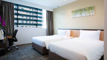 A hotel room with two beds, a desk with a chair, a window with curtains, and a painting on the wall.