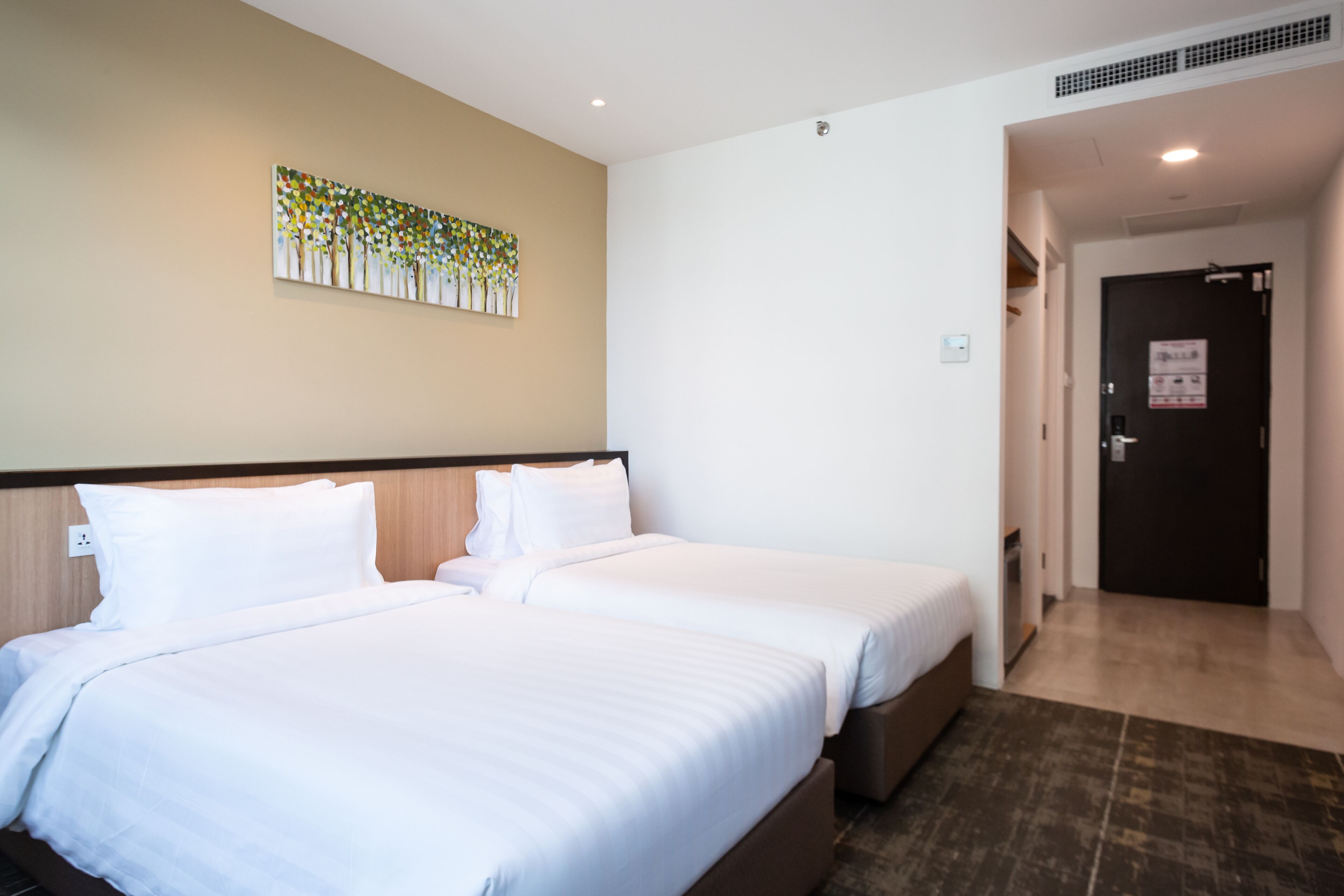 A hotel room with two beds, a beige wall, and a door leading to a hallway.