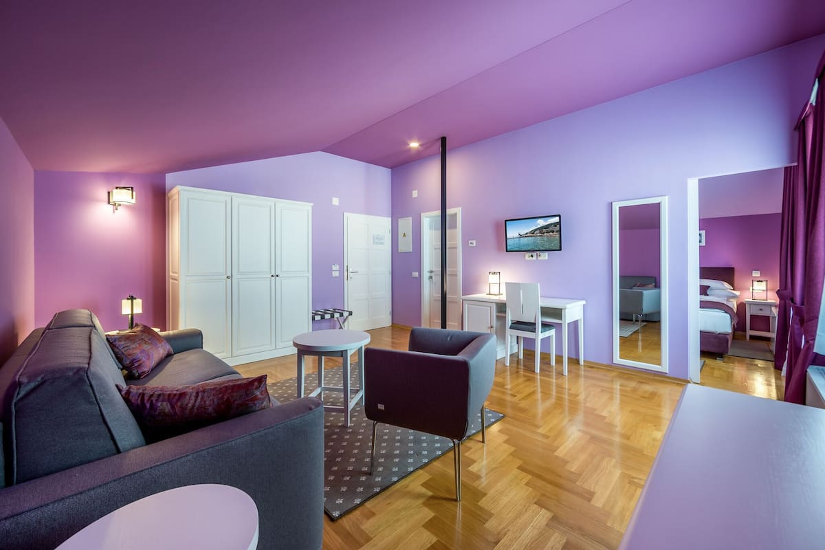 Ein modernes Wohnzimmer mit Sofa, Sessel und Couchtisch. Es gibt einen Essbereich mit Tisch und Stühlen, und ein an der Wand befestigter Fernseher.