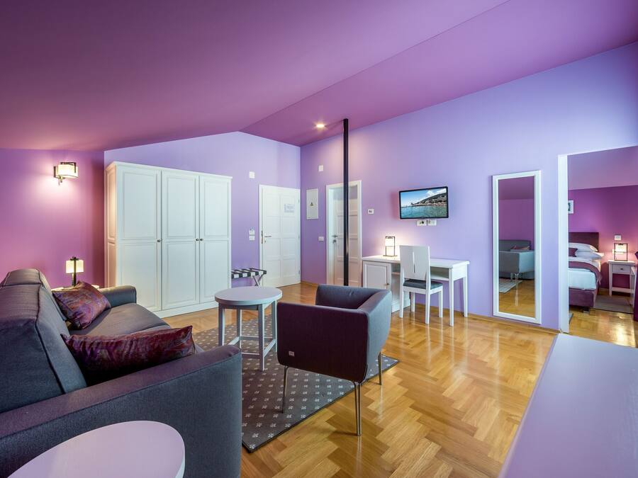 A modern living room with a sofa, armchair, and coffee table. There is a dining area with a table and chairs, and a TV mounted on the wall.