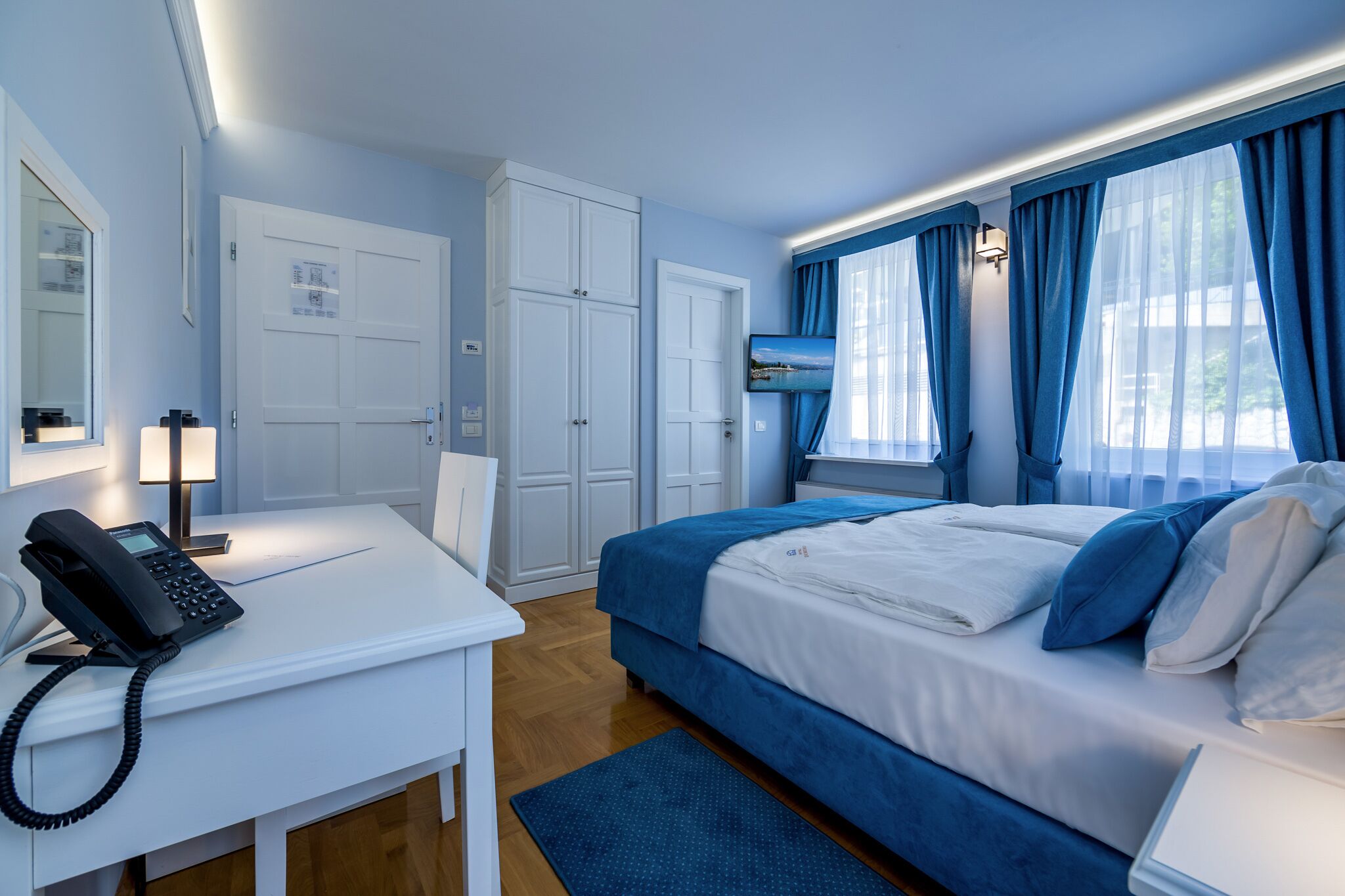 Ein Hotelzimmer mit Bett, Schreibtisch, Telefon, Stuhl und einem Fenster mit Vorhängen.