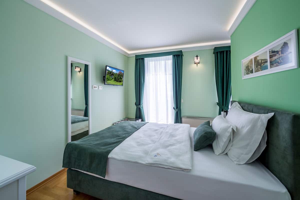 Ein Schlafzimmer mit Bett, Spiegel, Fernseher und einem Fenster mit Vorhängen.