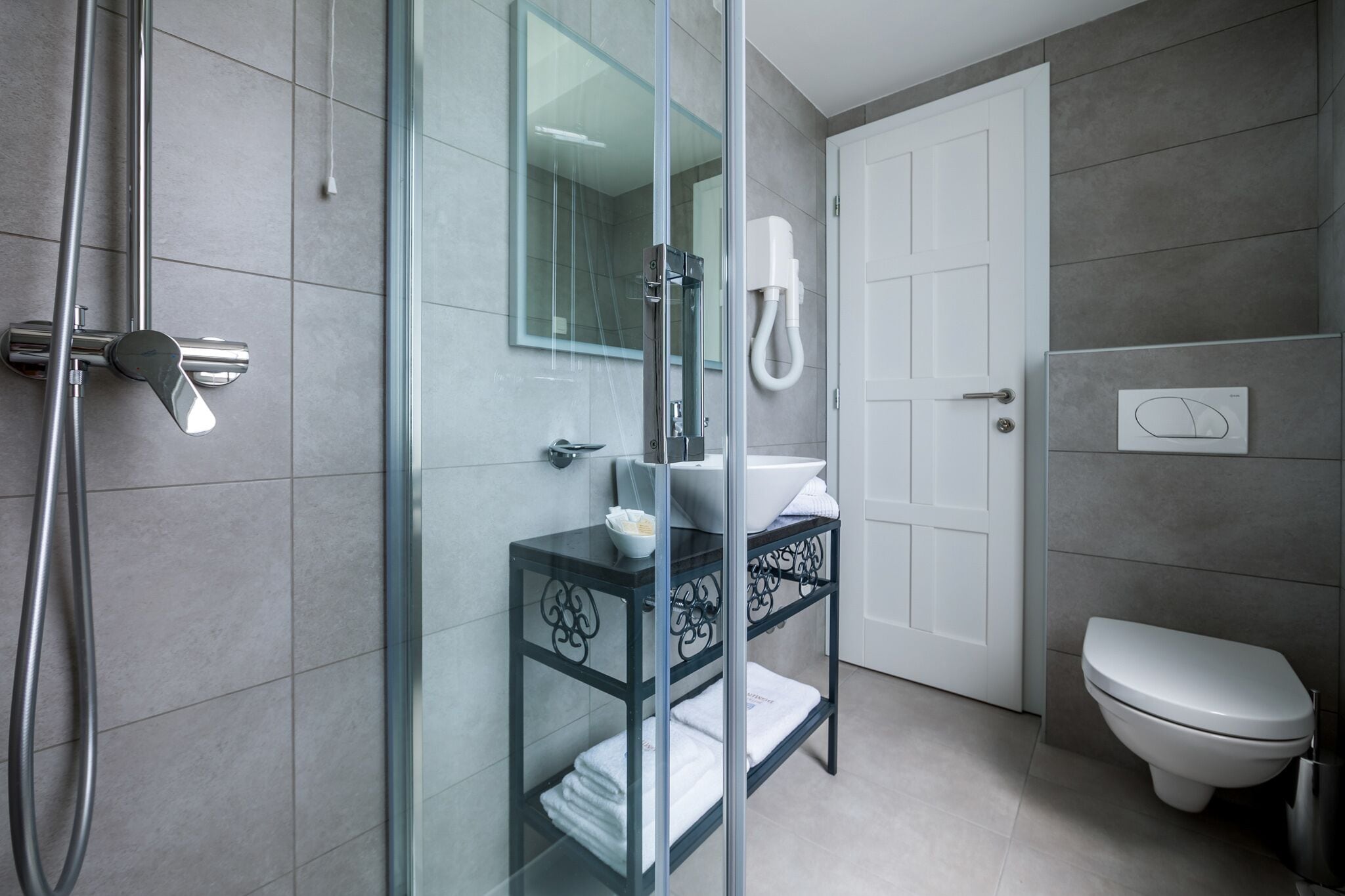 Ein modernes Badezimmer mit Duschkabine aus Glas, einer weißen Toilette und einem Waschtisch mit Spüle und Handtuchhalter.