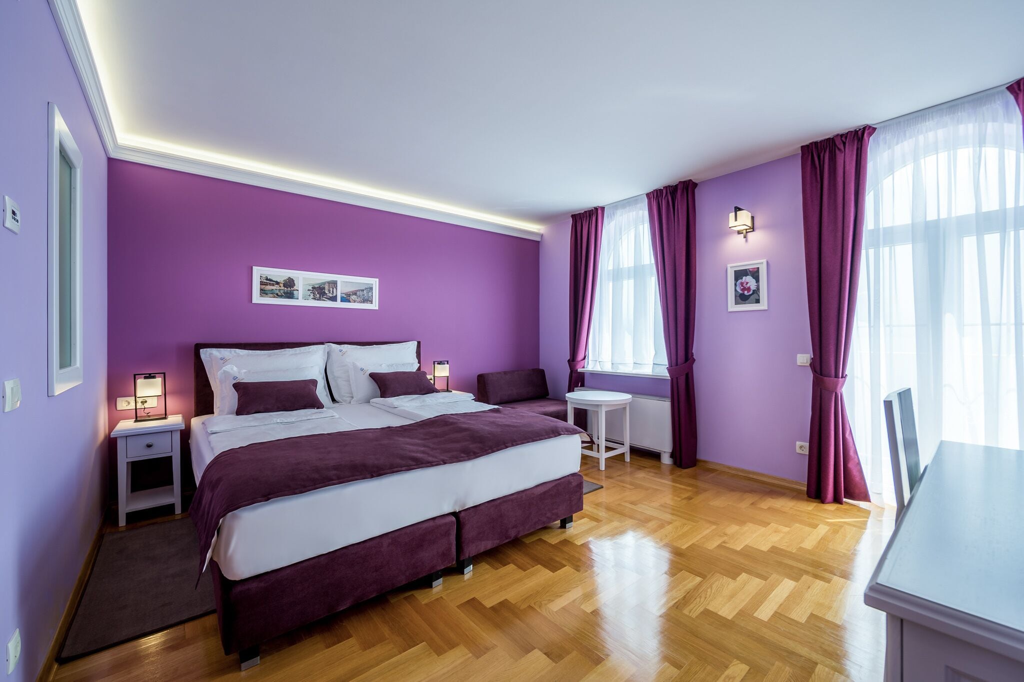 Un dormitorio con una cama grande, una mesita de noche, una pequeña mesa redonda y una ventana con cortinas.