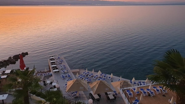 Un complejo turístico frente al mar con terraza, tumbonas y vista despejada al horizonte.
