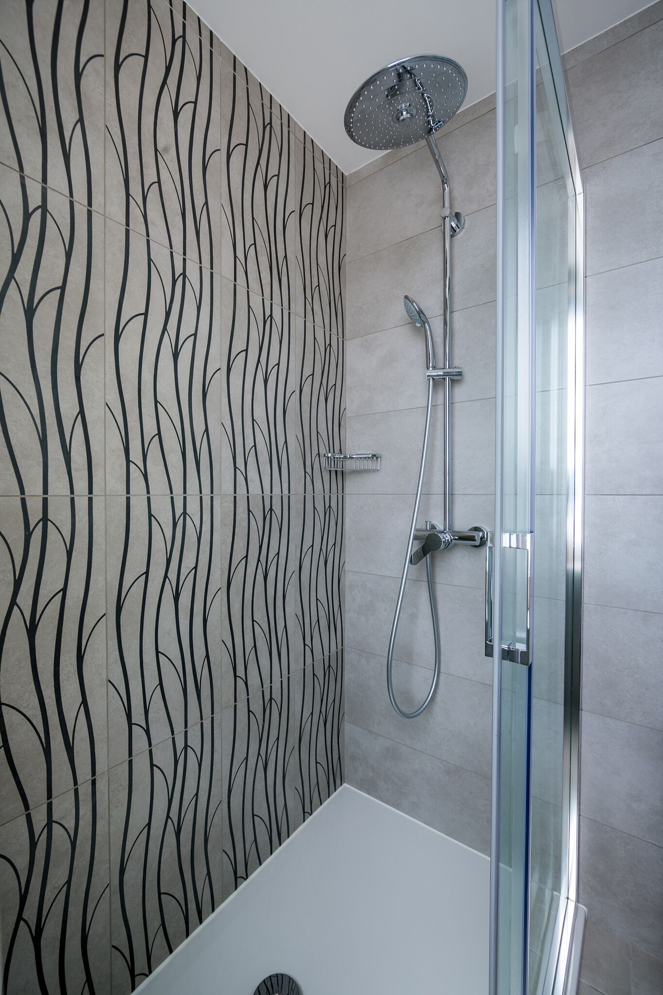 Une salle de bain moderne avec une douche à parois de verre, une baignoire blanche et un mur orné d’un motif ondulé.