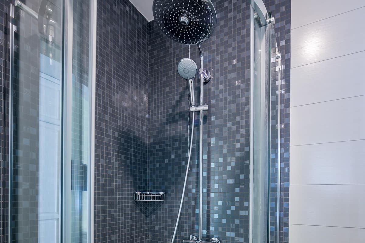 Eine Duschkabine mit Regendusche und Handbrause, Fliesenwänden und weißem Boden.