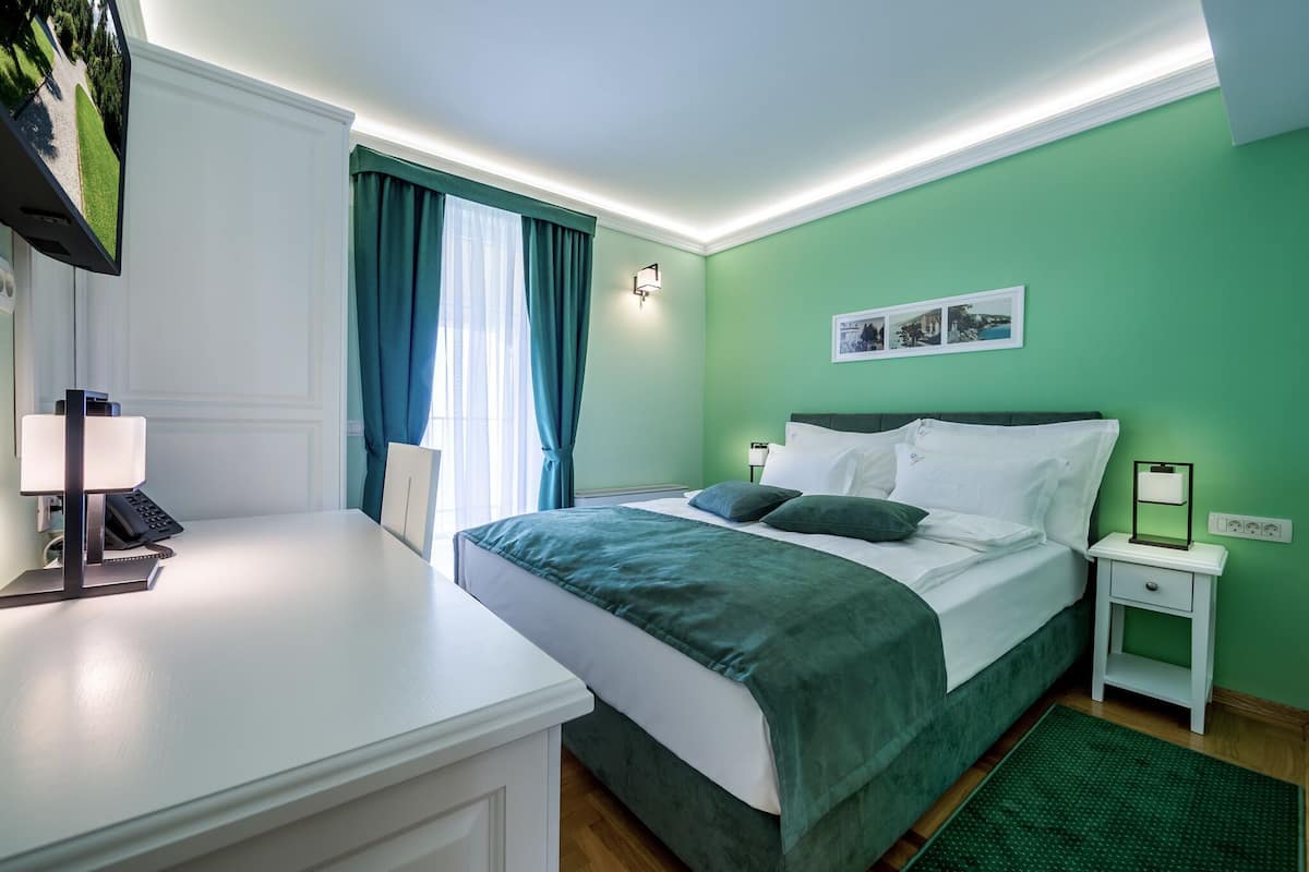 Ein ordentlich eingerichtetes Hotelzimmer mit Bett, Nachttisch, Lampe und Schreibtisch mit Telefon.