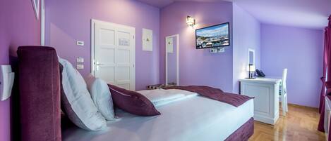 A bedroom with a large bed, a bedside table, a TV mounted on the wall, and a door with a sign.