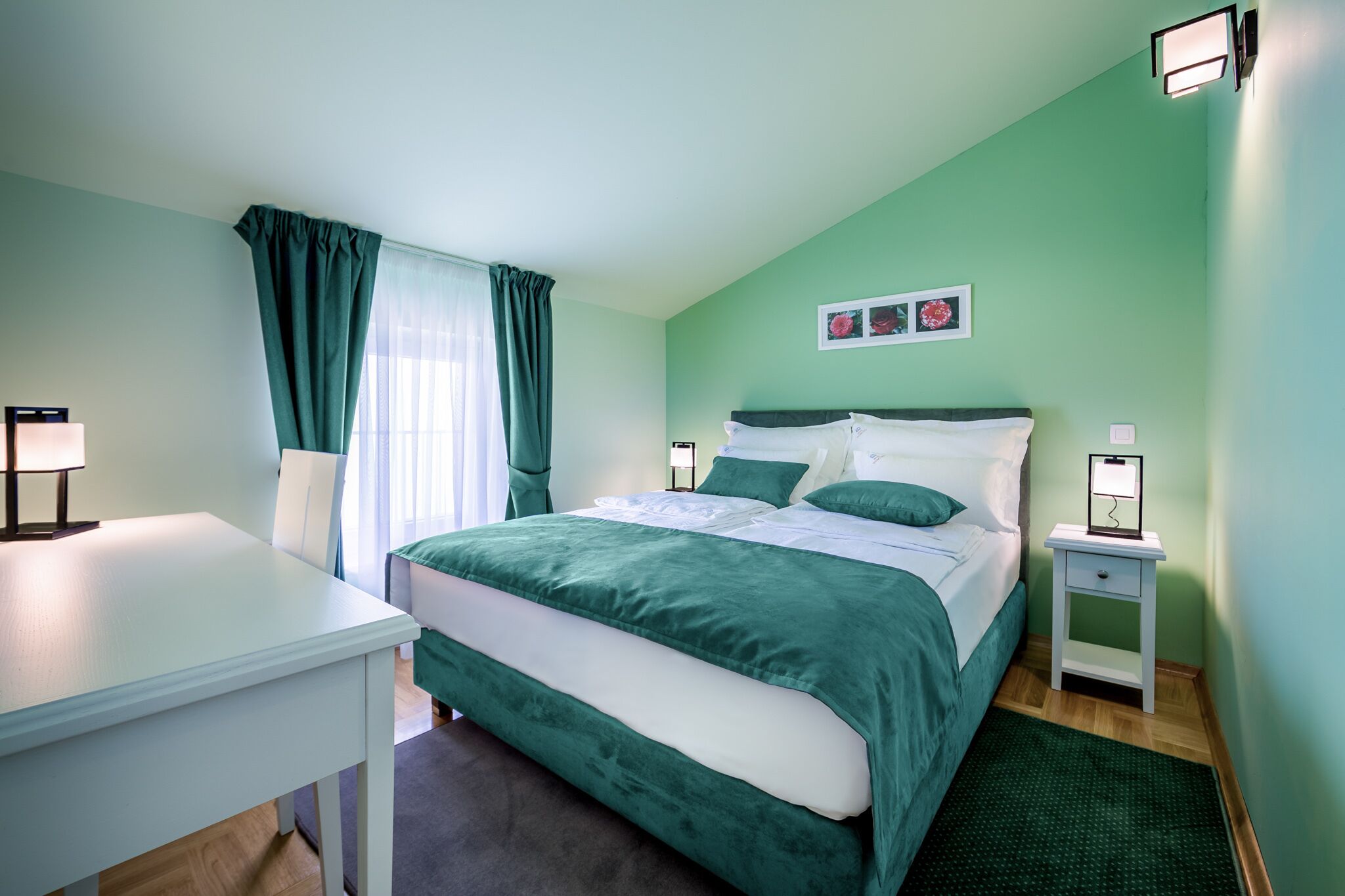 A neatly arranged bedroom with a bed, bedside tables, a desk, and a window with curtains.