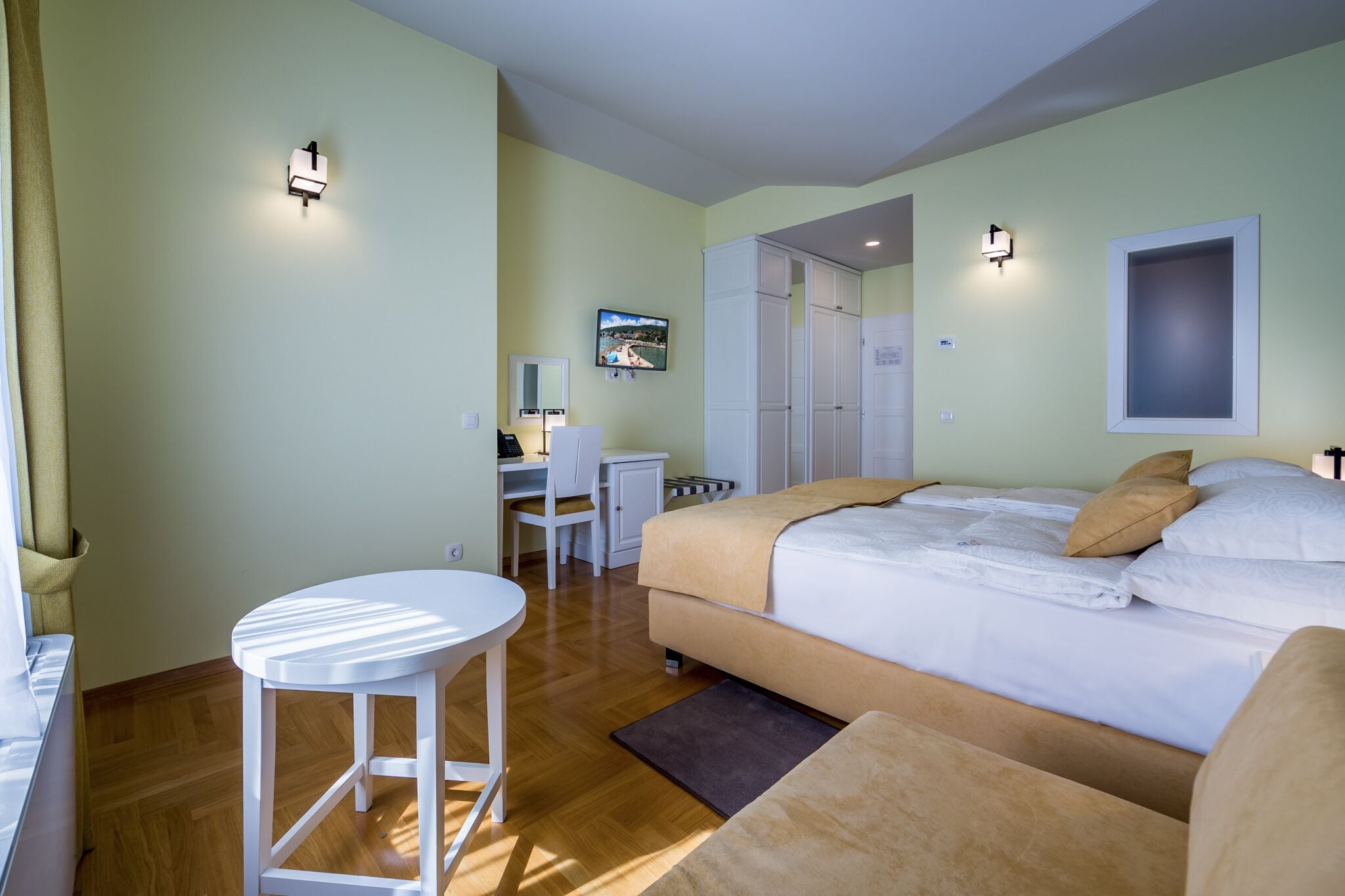 Un dormitorio con cama, mesita de noche y escritorio con silla. Hay un televisor montado en la pared y un armario.