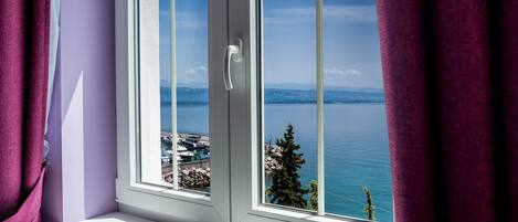 A window with a view of a coastal landscape, including a body of water and distant land.