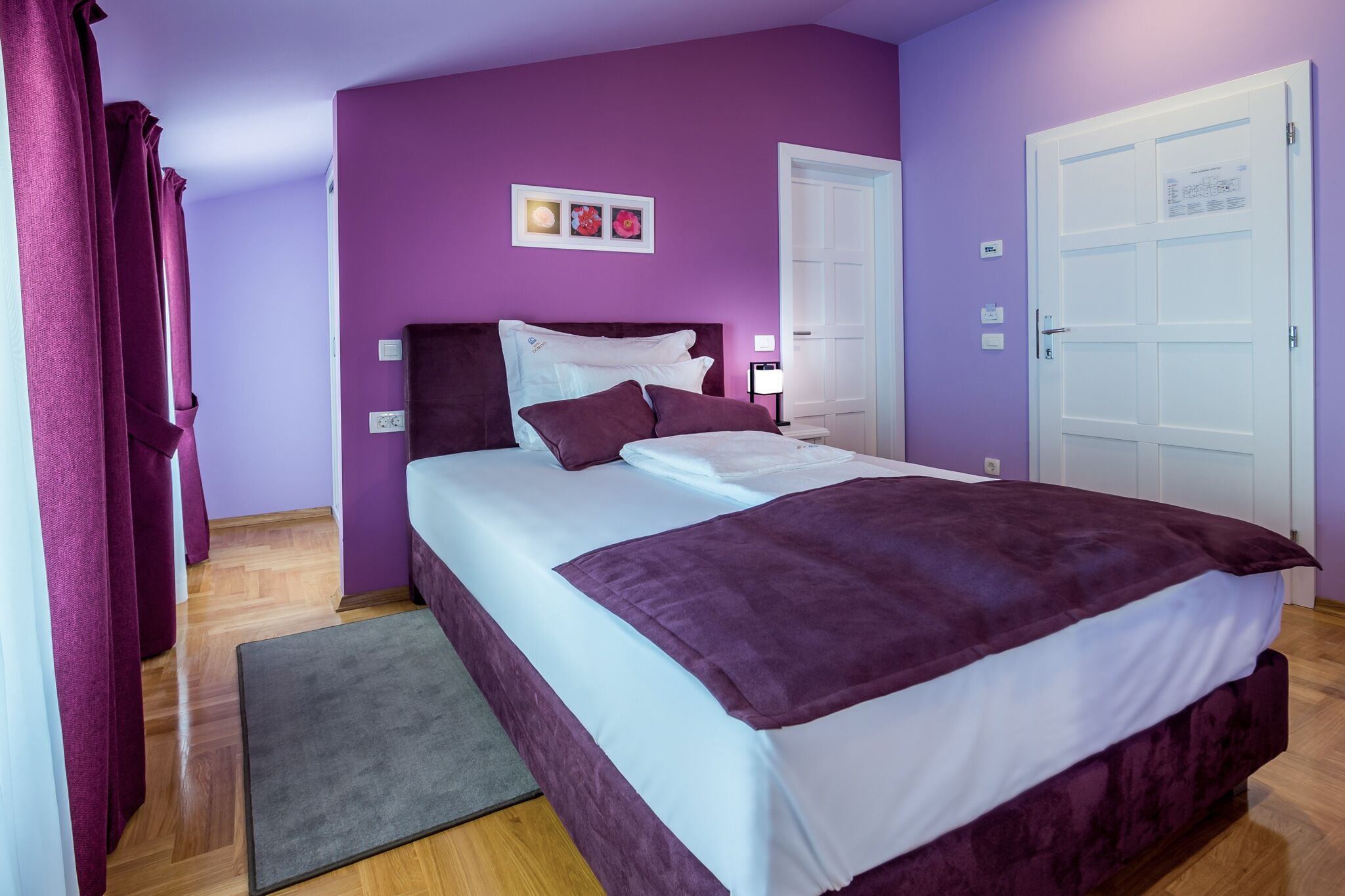 A bedroom with a bed, purple walls, a door, and a small rug.