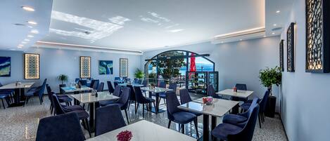 A modern dining area with multiple tables and chairs, a view of the outdoors, and decorative wall art.