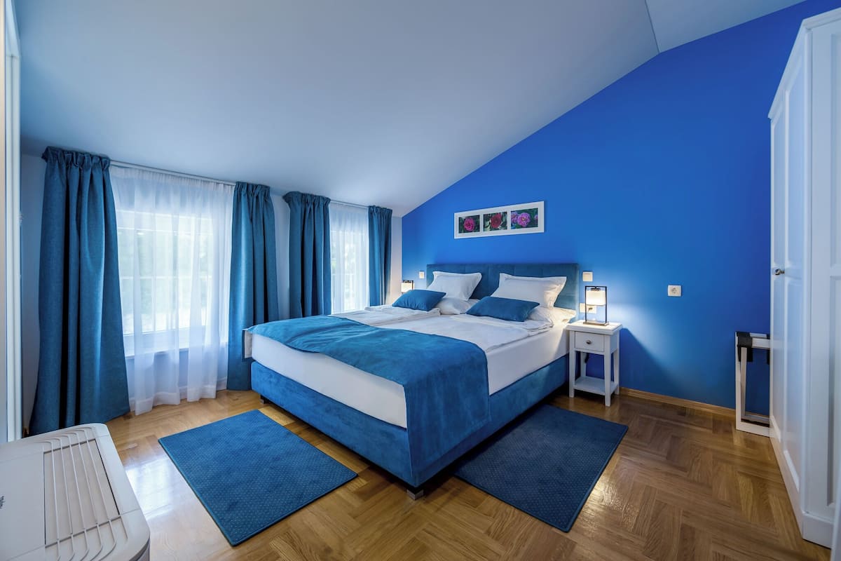 Ein Schlafzimmer mit einem großen Bett, einem Nachttisch mit Lampe und einem Fenster mit Vorhängen.
