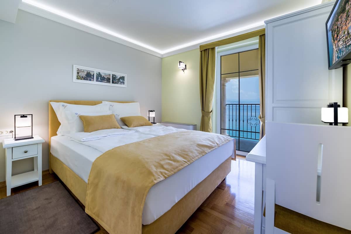 Ein Hotelzimmer mit Bett, Nachttischen, einem Kleiderschrank, einem Balkon mit Blick und einem an der Wand befestigten Fernseher.