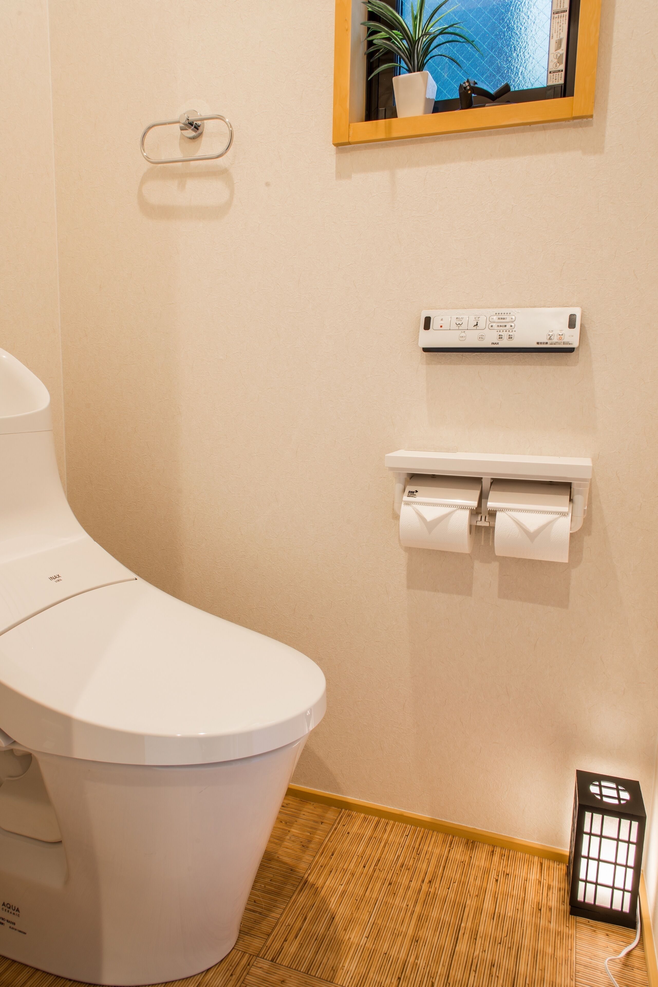 A modern bathroom with a white toilet, a toilet paper holder, a wall-mounted heater, and a small potted plant.