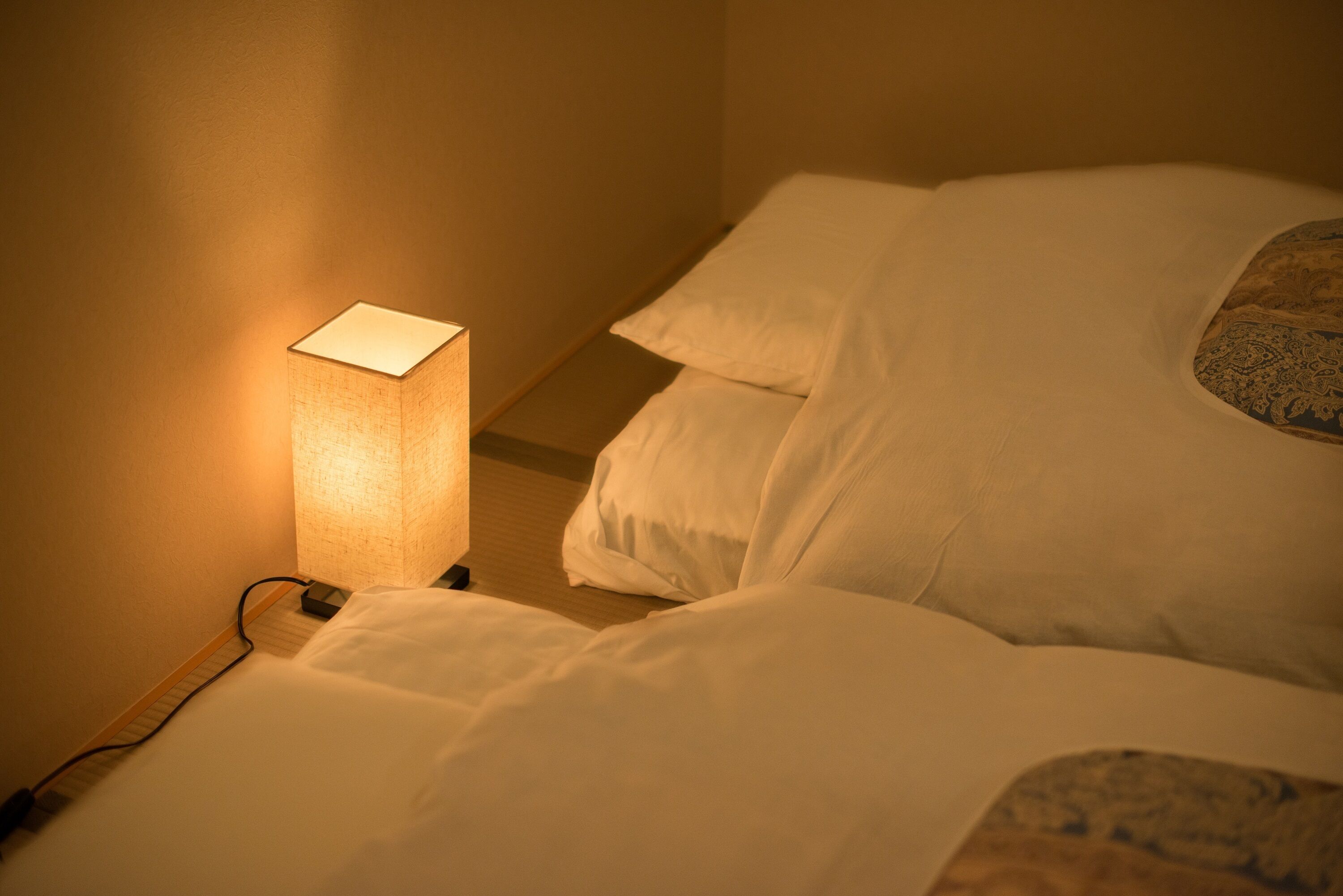 A neatly made bed with white linens and a single bedside lamp.