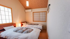 Et soveværelse med to senge, træloft, et vindue med et gittermønster og en vægmonteret aircondition.