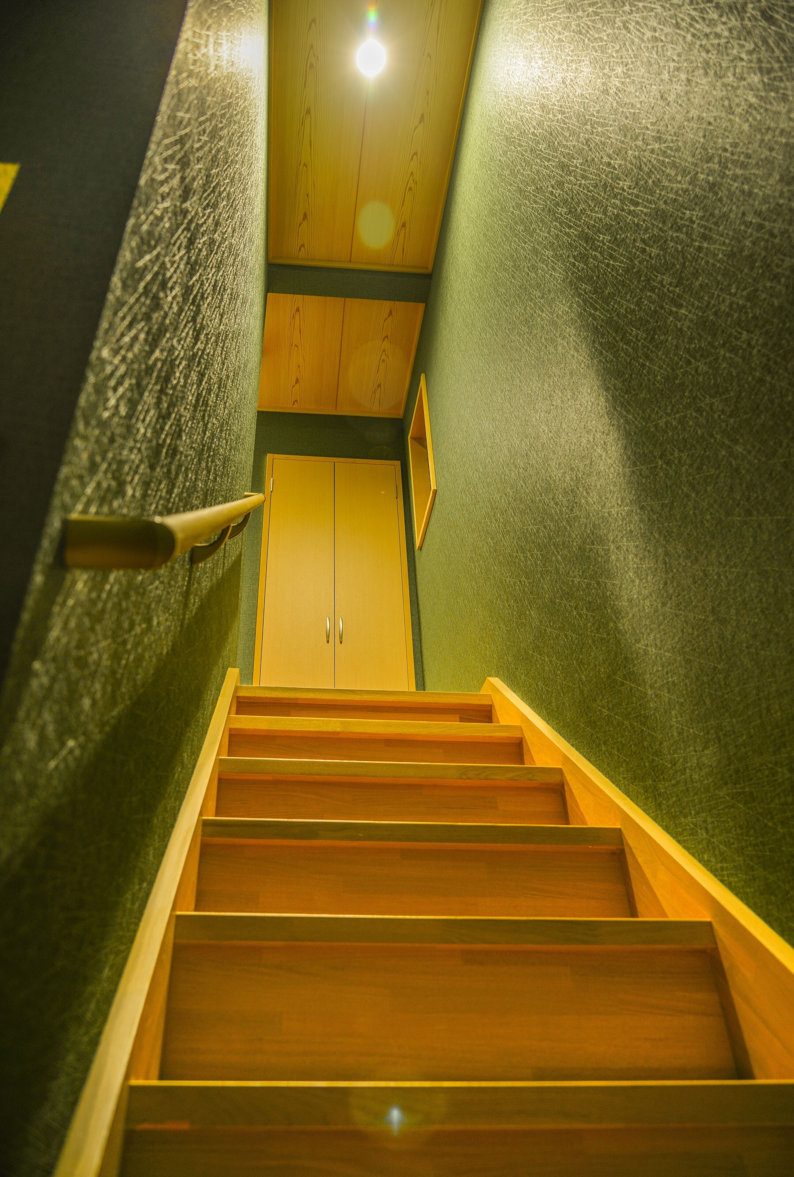 Una escalera de madera que conduce a una habitación con una pared verde y una puerta de madera.