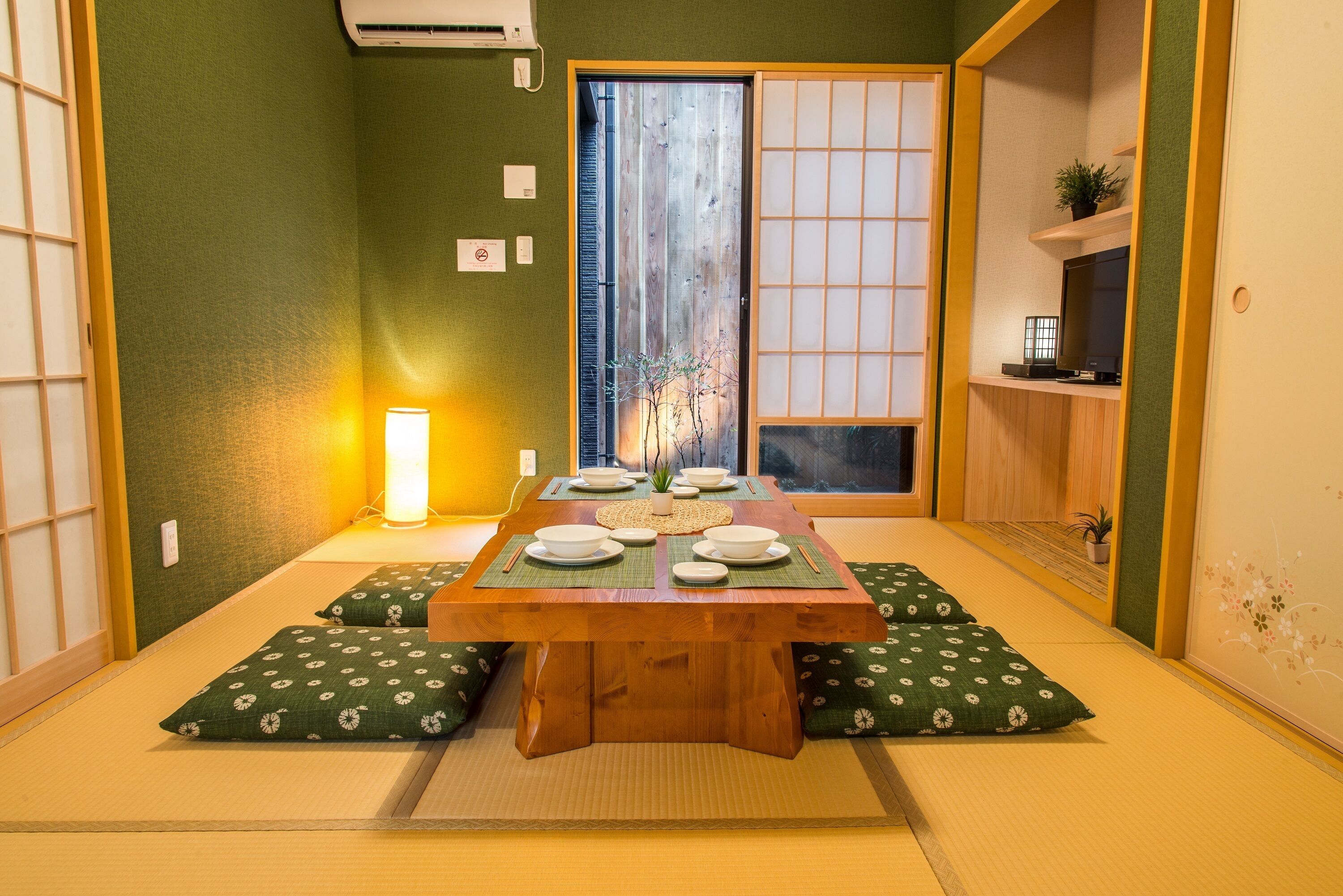 A traditional Japanese room with tatami flooring, a low wooden table set for a meal, and shoji screens.