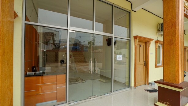 A hotel entrance with a glass door, a wooden reception desk, and a staircase leading to the upper floors. - OYO 1146 Miracle Homestay Syariah (Palembang)