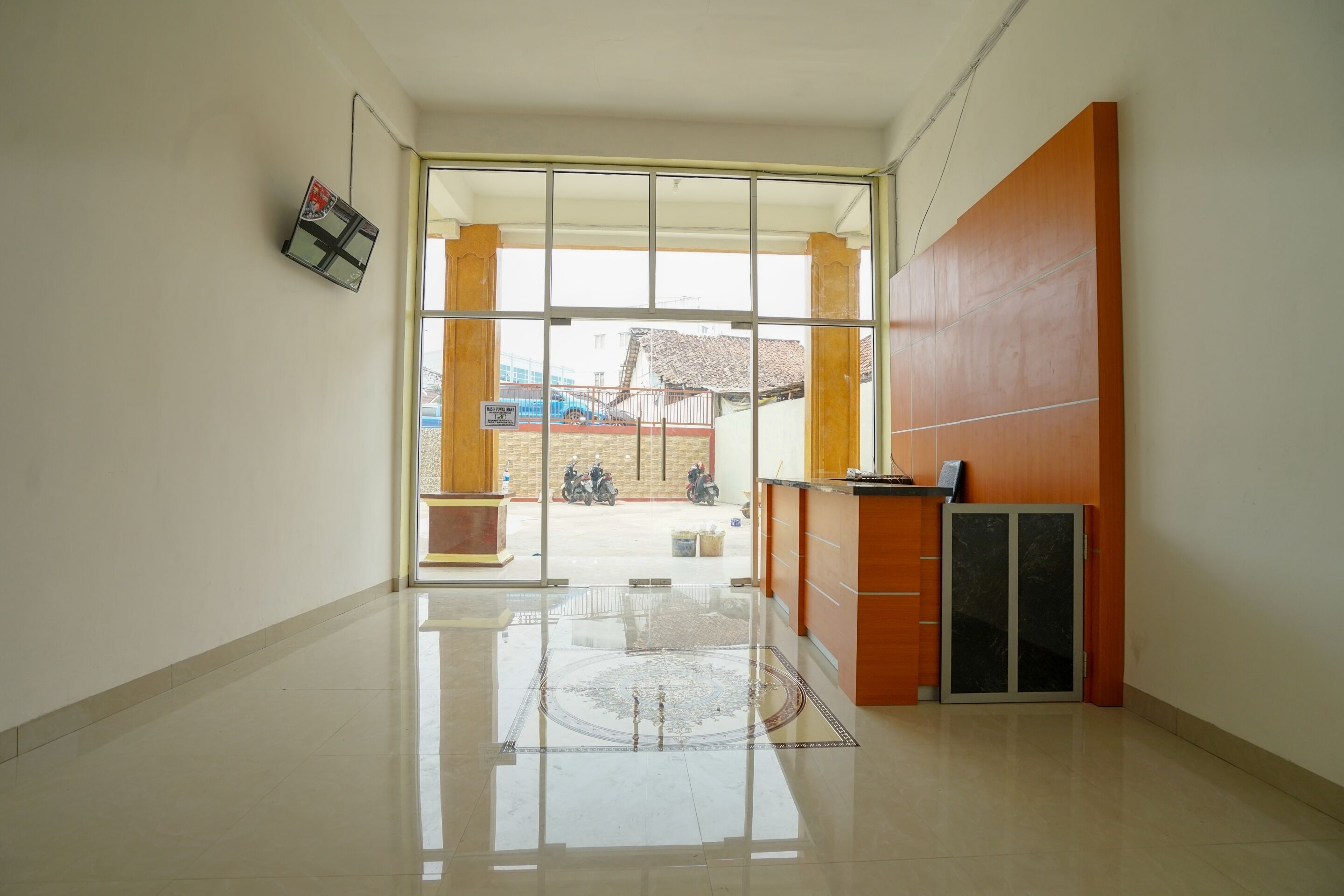 A spacious lobby with a large glass door leading outside, a reception desk, and a tiled floor.