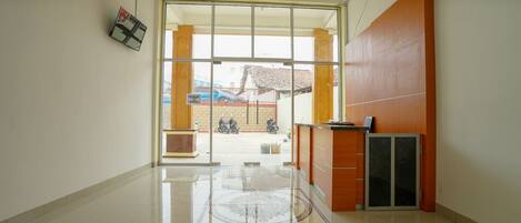 A spacious lobby with a large glass door leading outside, a reception desk, and a tiled floor.