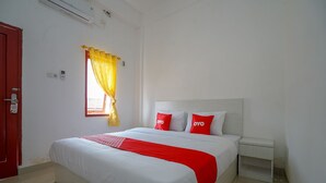 A hotel room with a large bed, white walls, a red door, and a window with yellow curtains. - OYO 1146 Miracle Homestay Syariah (Palembang)