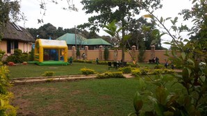 A grassy area with a play structure, a building with a green roof, and a stone wall. - Penthouse Inn (Moyo)