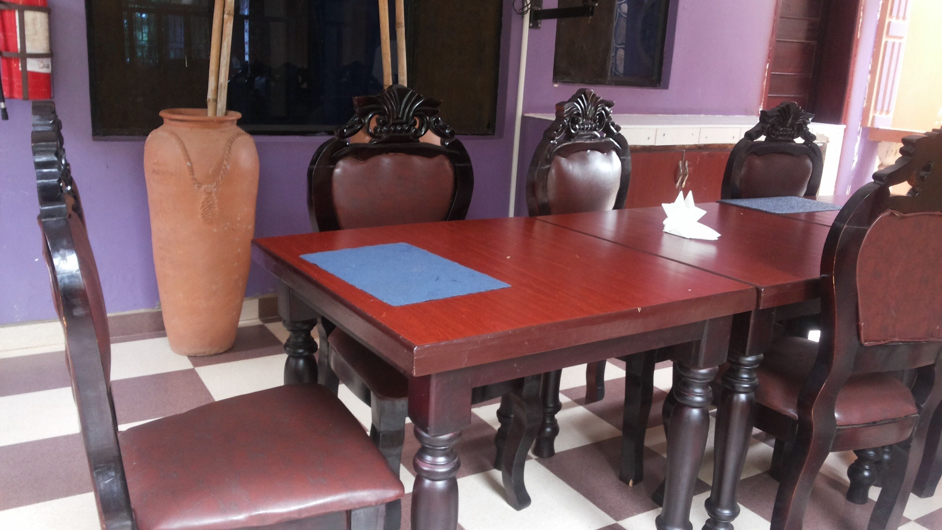 A dining area with a wooden table and chairs, a large vase, and a checkered floor.