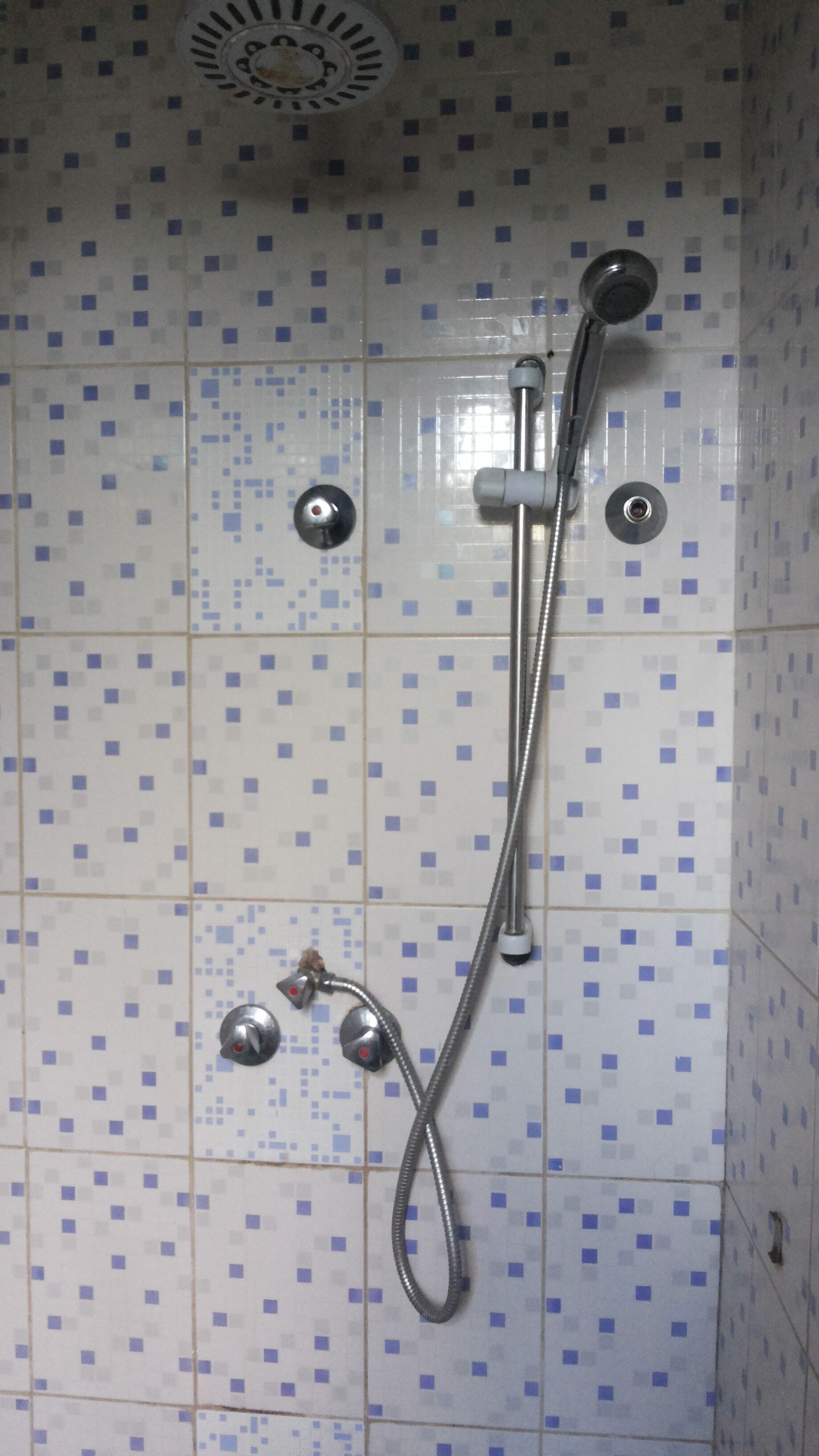 A shower with a handheld showerhead and a fixed overhead showerhead, both mounted on a tiled wall with a blue and white pattern.