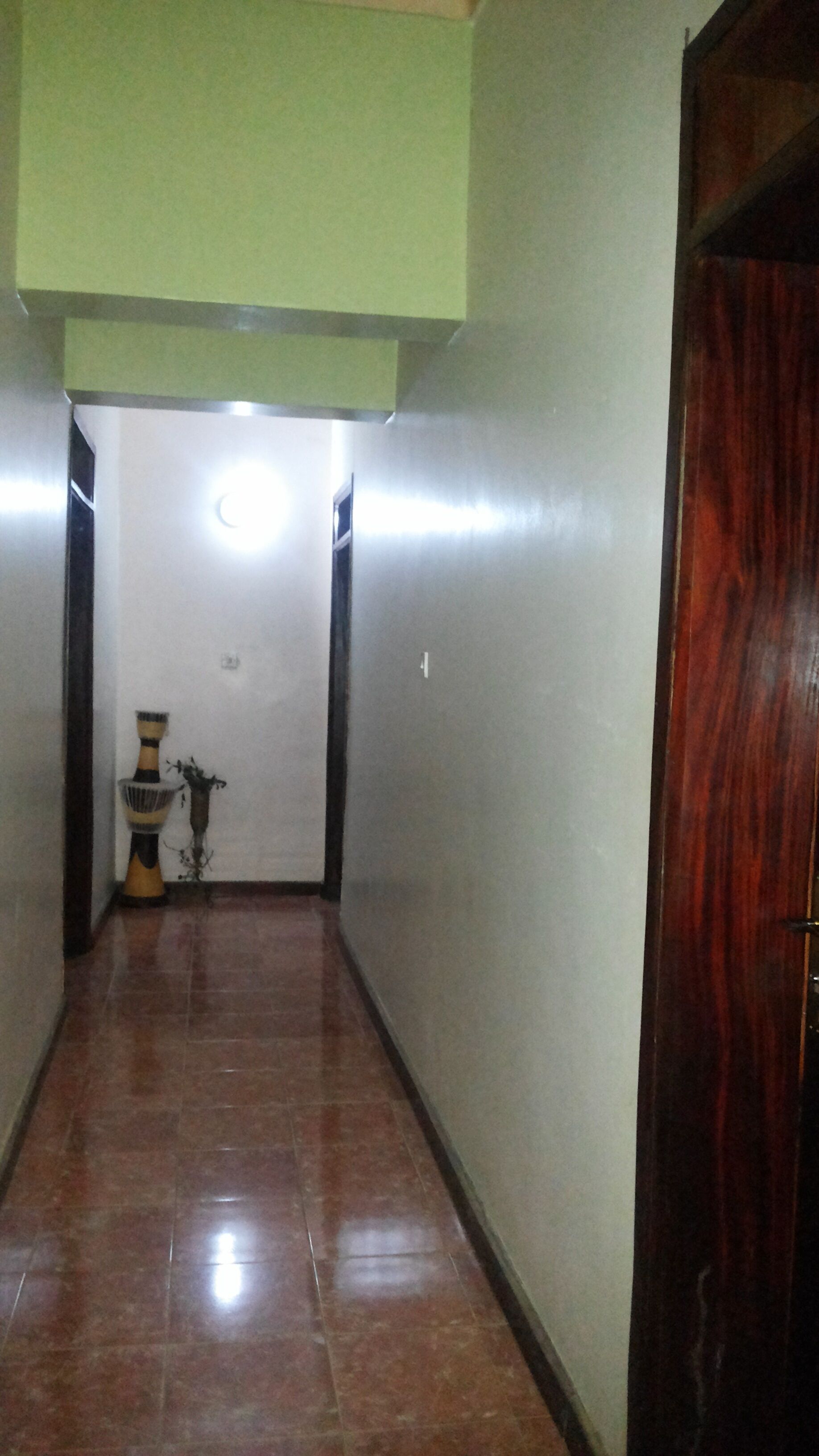 A hallway with a tiled floor, a wooden door on the right, and a light fixture on the wall.
