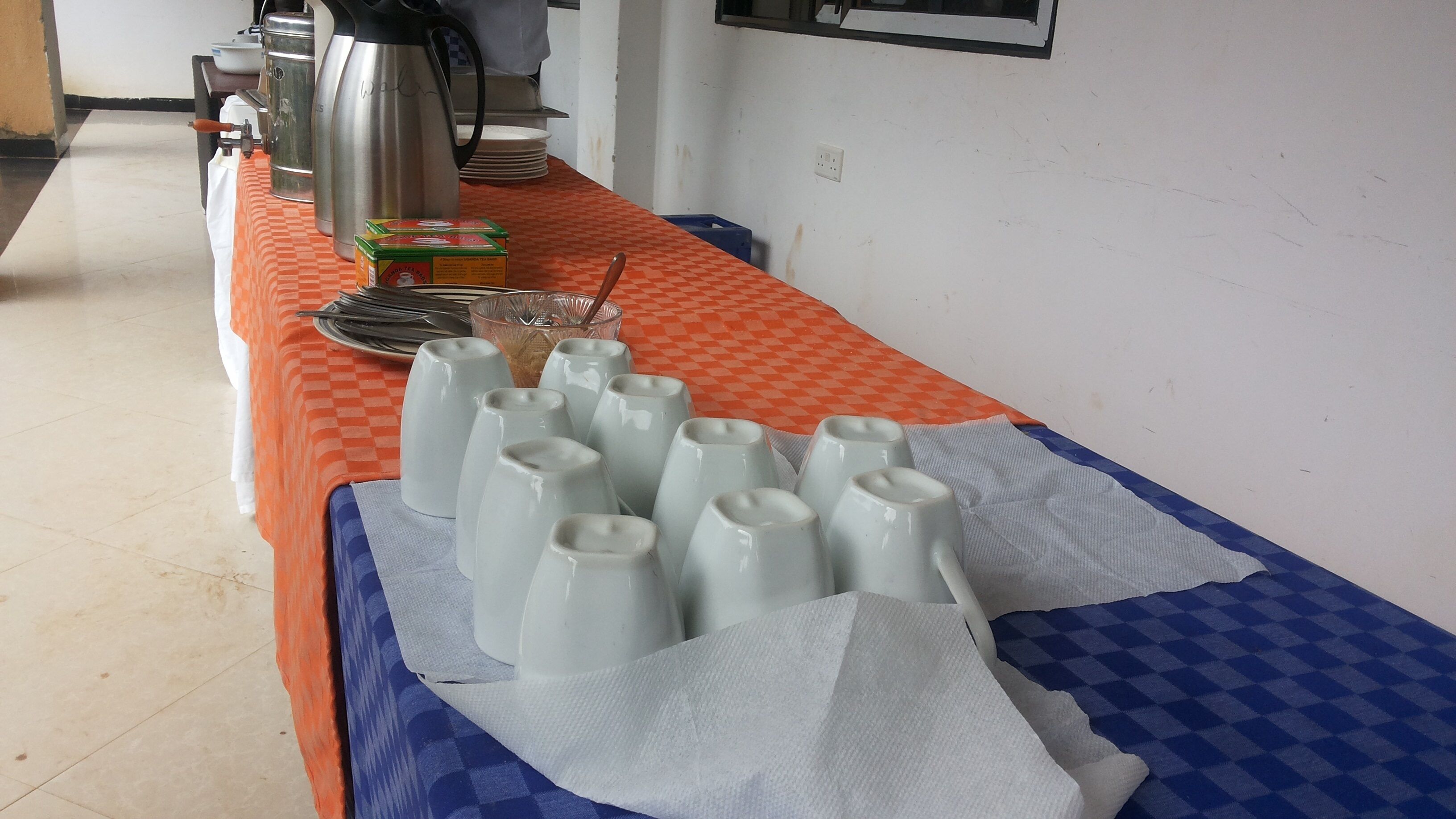 A table with a checkered tablecloth, a coffee pot, and several white cups lined up.