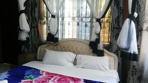 A bed with a floral bedspread, a headboard, and curtains with a floral pattern. - Penthouse Inn (Moyo)
