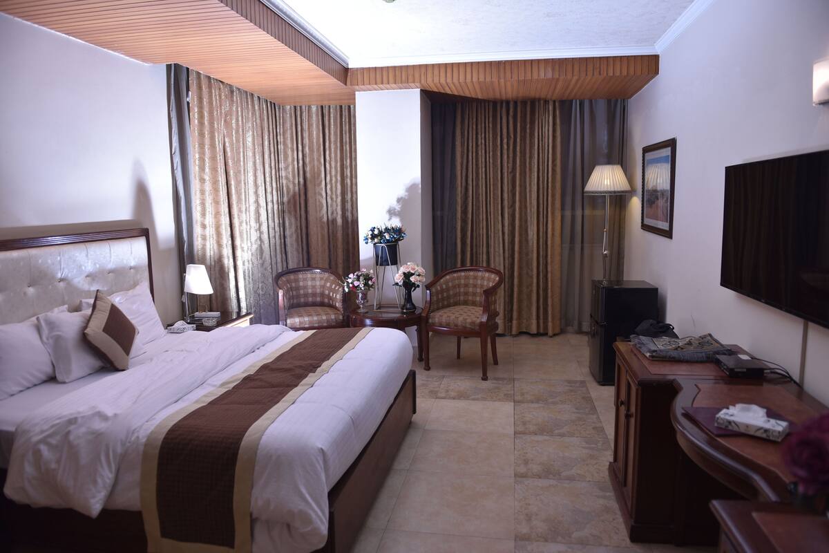 Una habitación de hotel con una cama grande, dos sillones, un escritorio, una lámpara y un televisor.