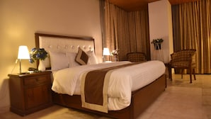 Una cama bien hecha con cabecera de madera, una mesita de noche con lámpara y una silla.