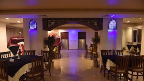 Un comedor de hotel con mesas y sillas, un arco central e iluminación decorativa.