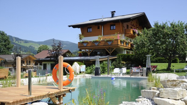 A hotel with a pool, wooden deck, and mountain views. - Landhaus & Haus Rustika (Wagrain)