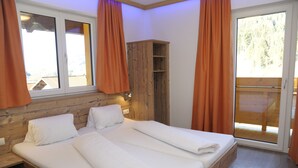 A bedroom with a wooden headboard, a large bed with white linens, a wardrobe, and a sliding glass door to a balcony. - Landhaus & Haus Rustika (Wagrain)