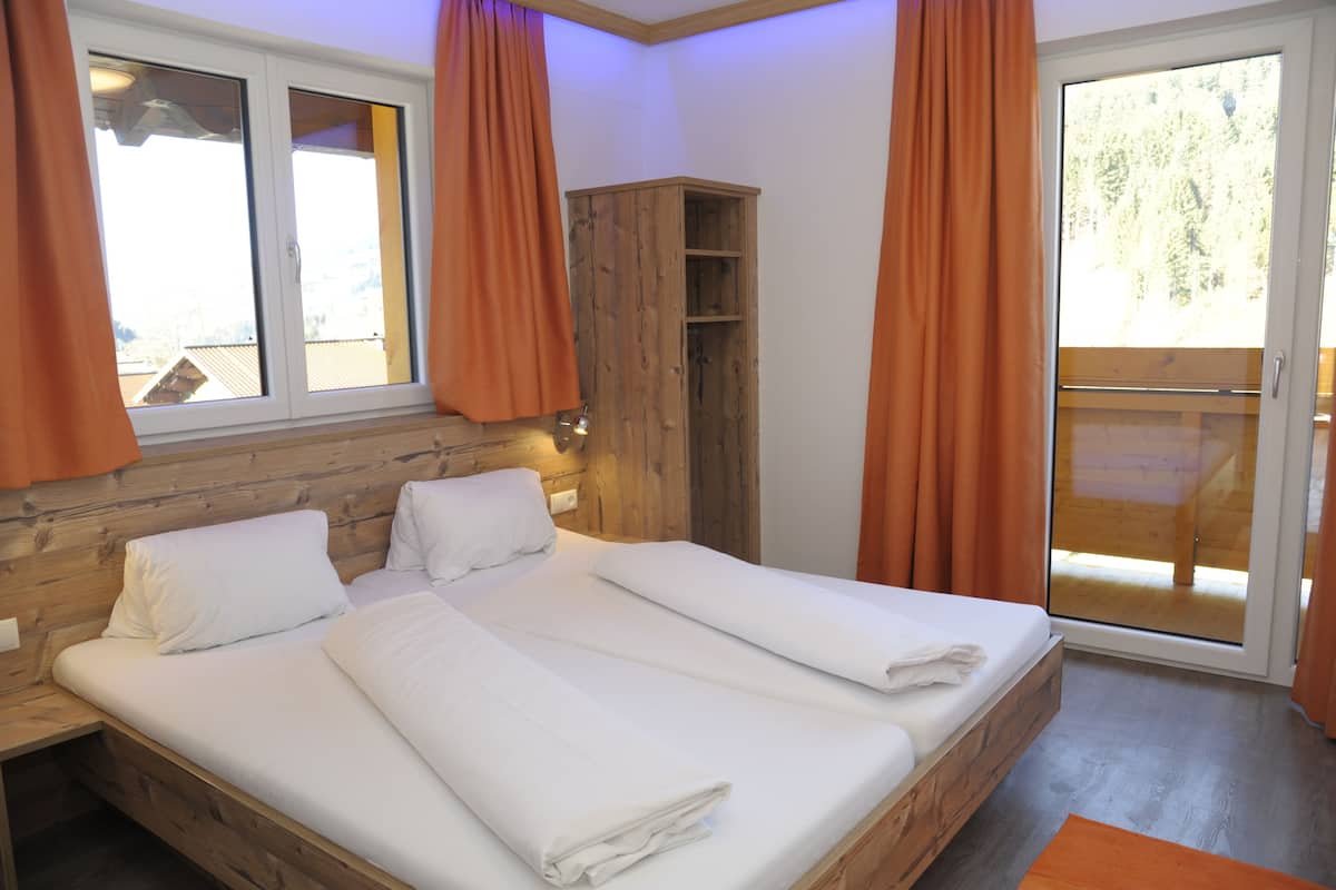 Un dormitorio con cabecera de madera, una cama grande con ropa blanca, un armario y un ventanal corredero a un balcón.