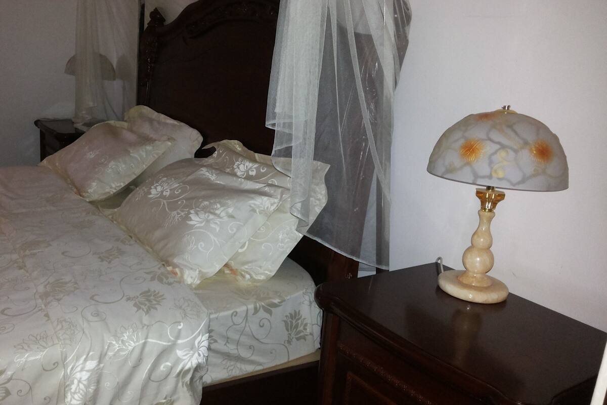 Ein Bett mit Baldachin, ein Nachttisch mit Lampe und ein Beistelltisch.